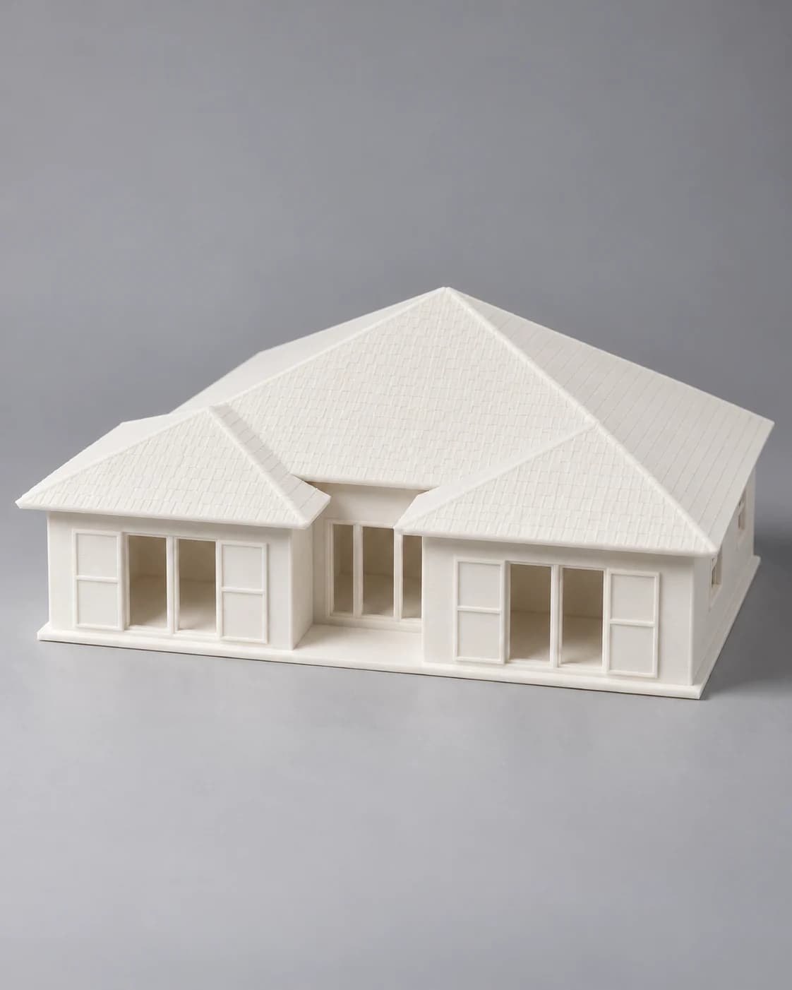 Front view of a white 3D-printed bungalow miniature with two hip-roofed wings, framed French doors and a recessed entrance